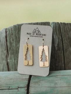 Two rectangular wooden earrings with pine tree silhouettes displayed on a card.