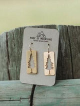 Two rectangular wooden earrings with pine tree silhouettes displayed on a card.