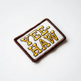 Embroidered patch with YEE HAW in bold yellow letters on white fabric with a brown edge