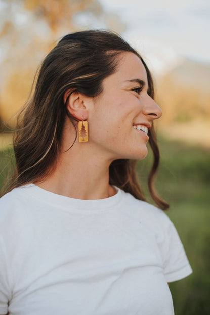 Woman outdoors wearing a rectangular wooden pine tree earring.