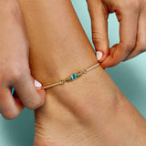 Close-up of a beige braided anklet with turquoise chips and gold spacers around the ankle.