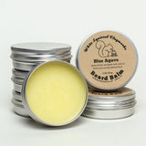 Stack of metal beard balm tins with an open tin in front showing pale yellow balm