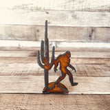 Rusty metal standee showing a tall saguaro cactus with a Bigfoot figure beside it.