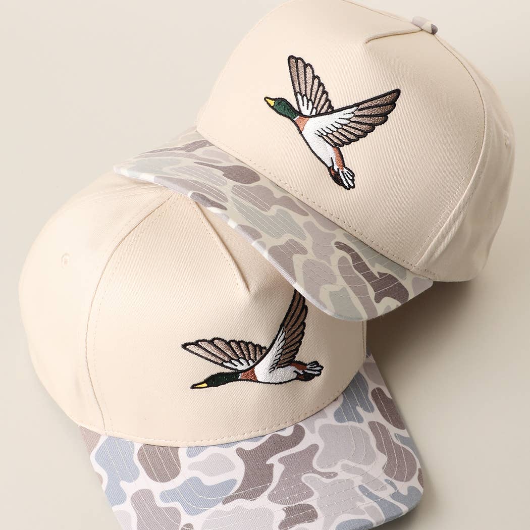 Beige Flying Mallard embroidered camo brim trucker hat worn by a man outdoors