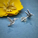 Silver hummingbird stud earrings with butterfly backs on a blue surface.