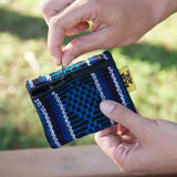 Close-up of hands unzipping a blue patterned recycled fibers coin purse outdoors