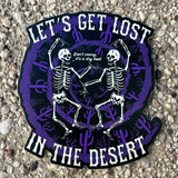 Let's Get Lost In The Desert sticker with two skeletons dancing inside a purple circular desert scene.
