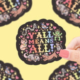 Hand holds a round black sticker with colorful YALL MEANS ALL text and cute forest animals on a yellow background