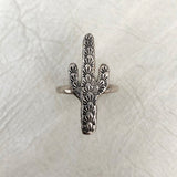 Silver ring shaped like a three armed cactus with engraved sunburst patterns along the arms.