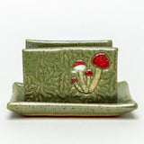 Green speckled ceramic sponge tray with a raised red mushroom relief on the front panel.