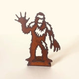 Rusty brown metal cutout standee of a waving Bigfoot on a rectangular base.