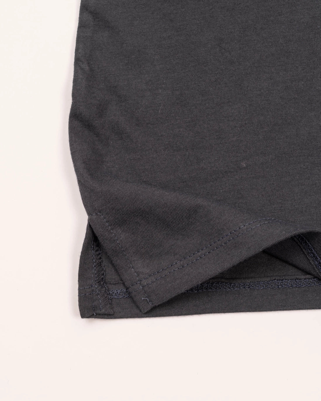 Bottom hem close up of charcoal tank showing reinforced stitching and a small green tag
