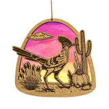 Wooden roadrunner ornament with desert scene including a cactus and pink sunset behind