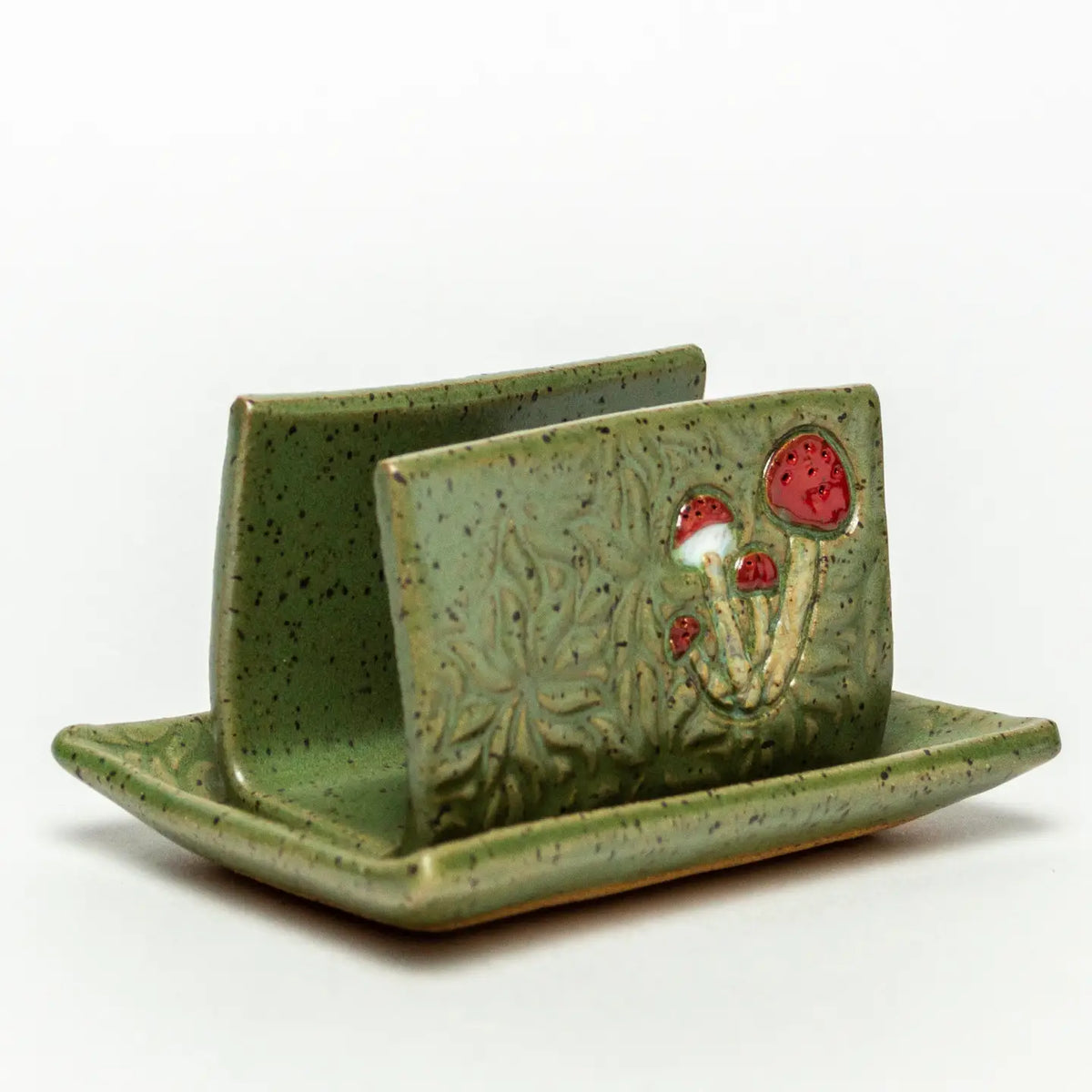 Front view of a green speckled ceramic tile with red mushroom relief resting on a matching sponge tray.