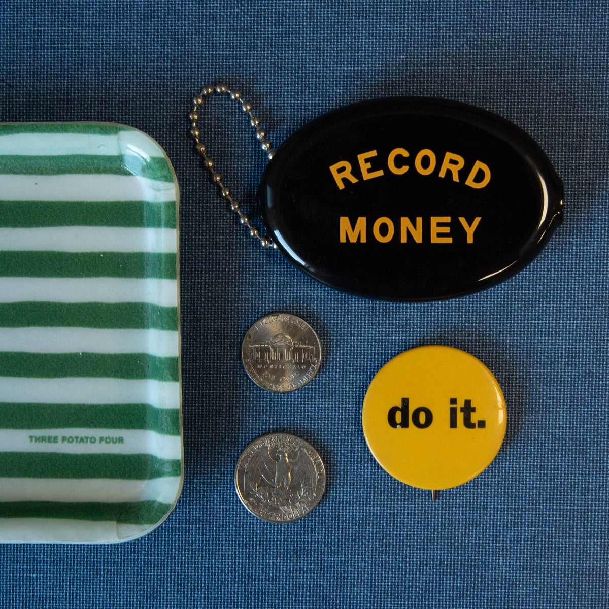 Blue denim backdrop with a round navy coin pouch labeled RECORD MONEY and loose coins nearby.