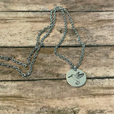 Round silver hummingbird pendant on a silver chain laid on a wooden surface
