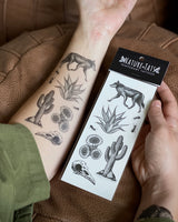 Forearm with desert themed temporary tattoos from The Wild Desert sheet showing wolf cactus agave and skull motifs.