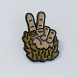 Enamel pin depicting a raised peace sign formed by a shaggy brown Bigfoot hand