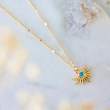 Gold chain necklace with turquoise starburst pendant on a marble background