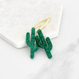 Green glitter cactus earrings on gold hoops with bold sparkle.