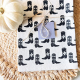 Cotton Western Boots Tea Towel with repeating black boot print and a lavender tag beside a white pumpkin.