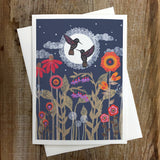 Greeting card with a dark blue night scene of a large lace moon and two hummingbirds among colorful flowers.