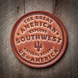 Circular brown leather coaster embossed with The Great American Southwest and a cactus symbol.