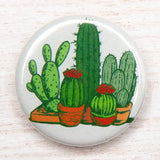 Round pin showing a cluster of green cacti in pots against a light background