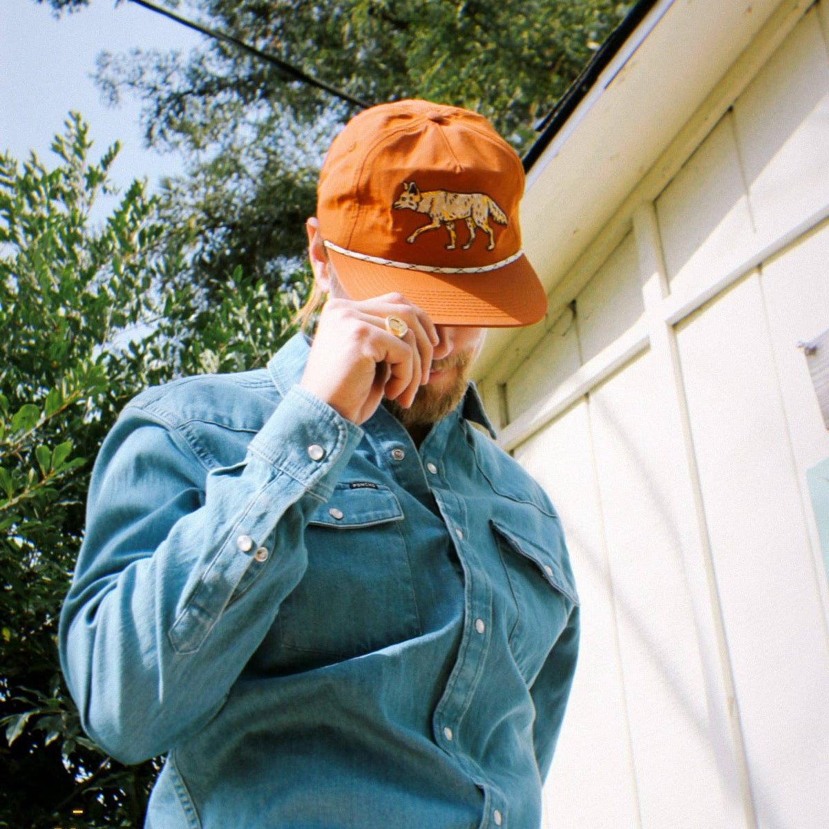 Orange coyote hat with a walking coyote embroidery and a white braided band worn over a blue denim shirt