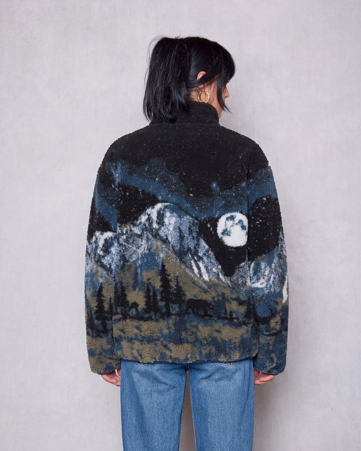 Back view of a model wearing a Yosemite Night Views full zip high pile unisex fleece with a mountain forest print