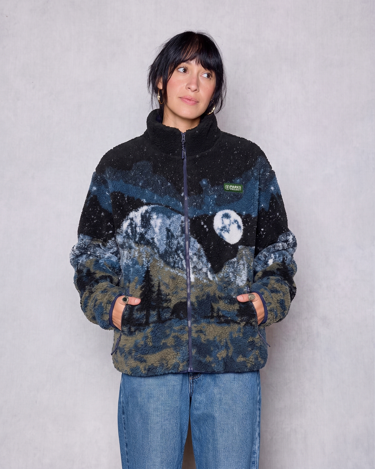 Model wearing Yosemite Night Views Full Zip fleece with mountain print in dark blue and tan with Parks Project patch