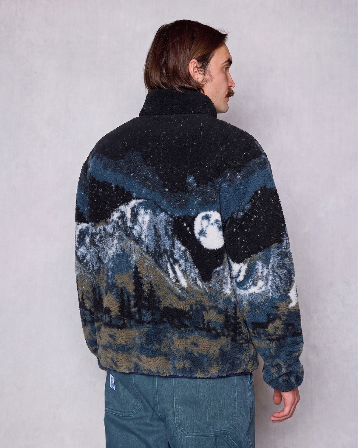 Back view of a man wearing a Yosemite Night Views fleece with a mountain landscape print and sherpa texture