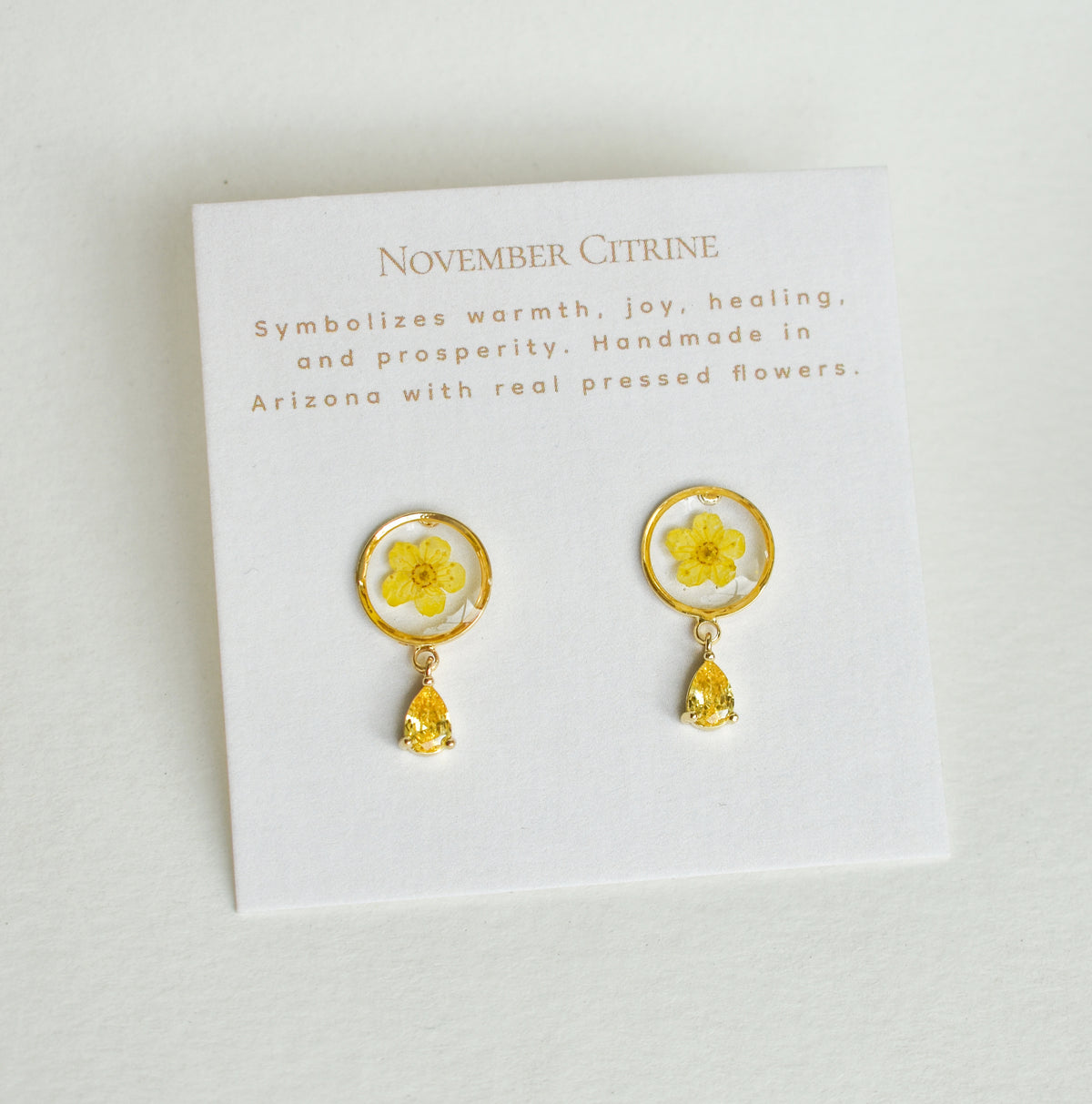 November Citrine birthstone earrings featuring pressed yellow flowers in gold circular settings with a matching teardrop charm on a card