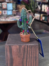 Glittery saguaro cactus ornament with multicolored lights and a twine hanger in a terracotta pot