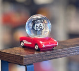 Glitter Route 66 globe perched on a small red toy car with a blurred background