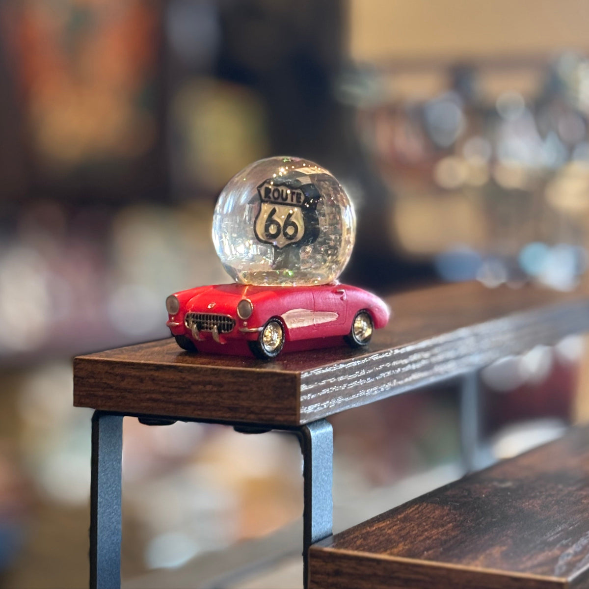 Route 66 glitter globe perched on a red toy car against a blurred background