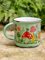 Mint green Camp Coffee Mug with a colorful mushroom and flower design resting on a stone surface outdoors.