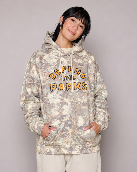 Front view of Defend the Parks Bear Hoodie in beige camouflage with orange logo on the chest worn by a model