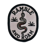 Round white patch with a black border and embroidered snake design and Ramble and Roam lettering