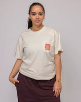 Cream Rooted in Nature pocket tee worn by a woman with a colorful floral print on the chest pocket