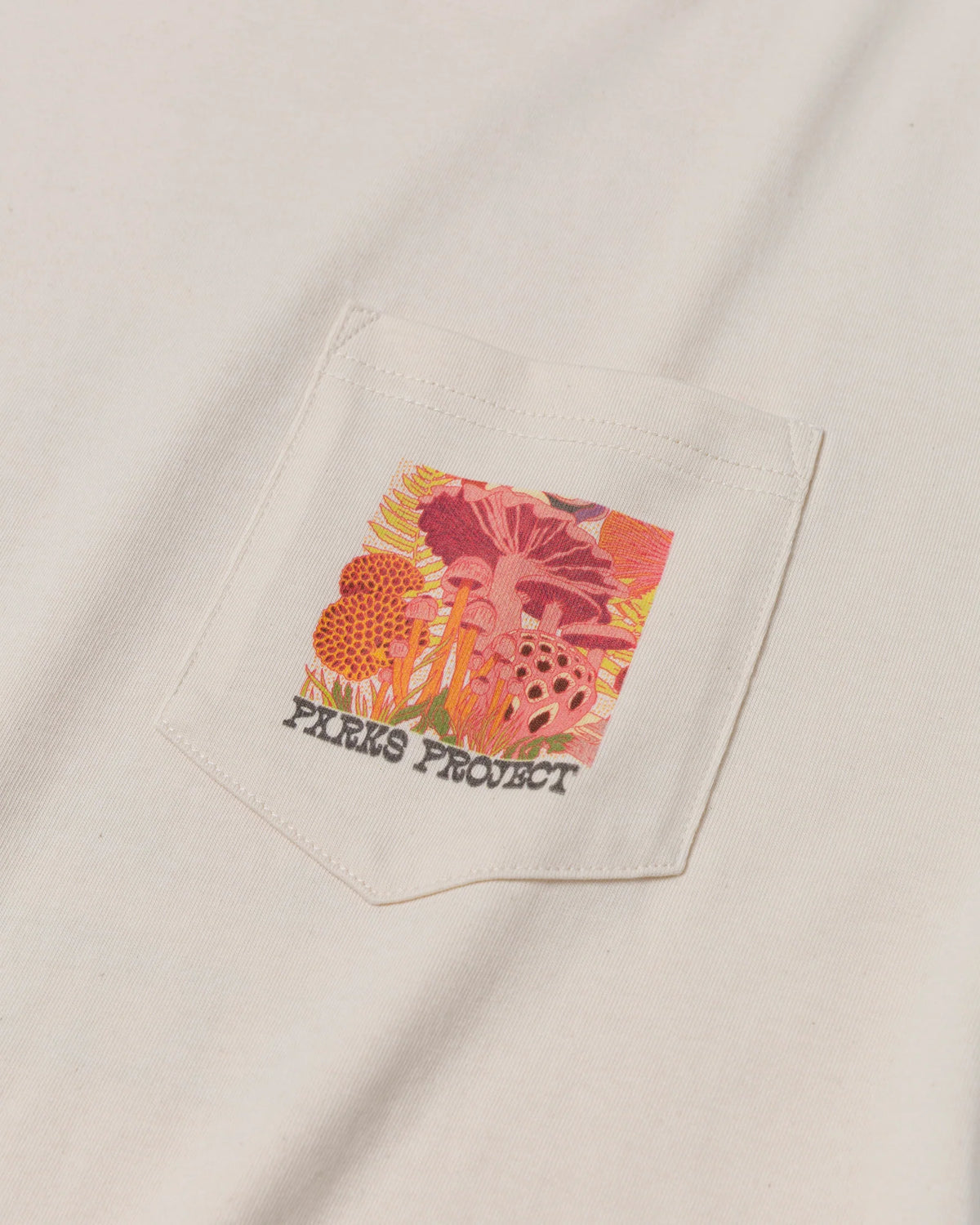 Cream pocket tee with a bright floral patch peeking out from the pocket.