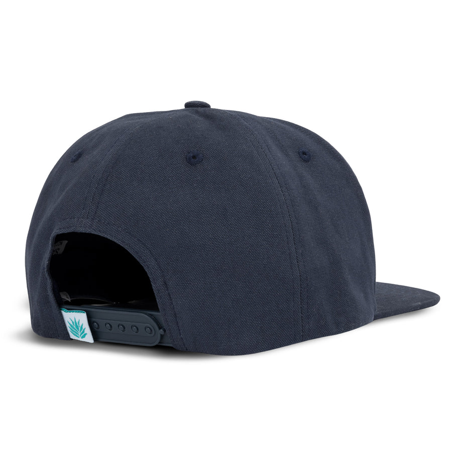 So Bueno navy flat brim hat viewed from the back with an adjustable snap strap and teal leaf tag.
