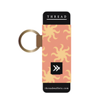 Thread patterned lip balm holder in pink fabric with yellow sunburst motif and a gold key ring