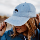 Close up of light blue denim Three Trees Relaxed Trucker hat with black tree logo being adjusted by a person.