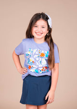 Smiling girl in a lavender blossom and bloom graphic kids tee with a dark blue skirt.