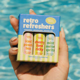 Hand holding blue Retro Refreshers lip balm trio box with three pastel balms visible.