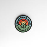 Circular embroidered patch with blue sky, rainbow rings over green mountains, and the border text EVERYTHING HURTS HIKING CLUB.