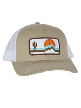 The Retrozona Trucker hat in tan with white mesh and a brown edged desert patch featuring cactus and mountains at sunset.