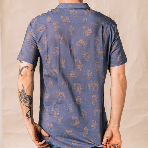 Back view of a man wearing the blue Adios Burritos Casual Button Down with tan desert print.