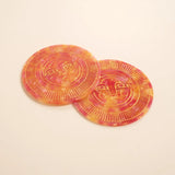 Two pink orange marbled coasters with a sun face design on a light background